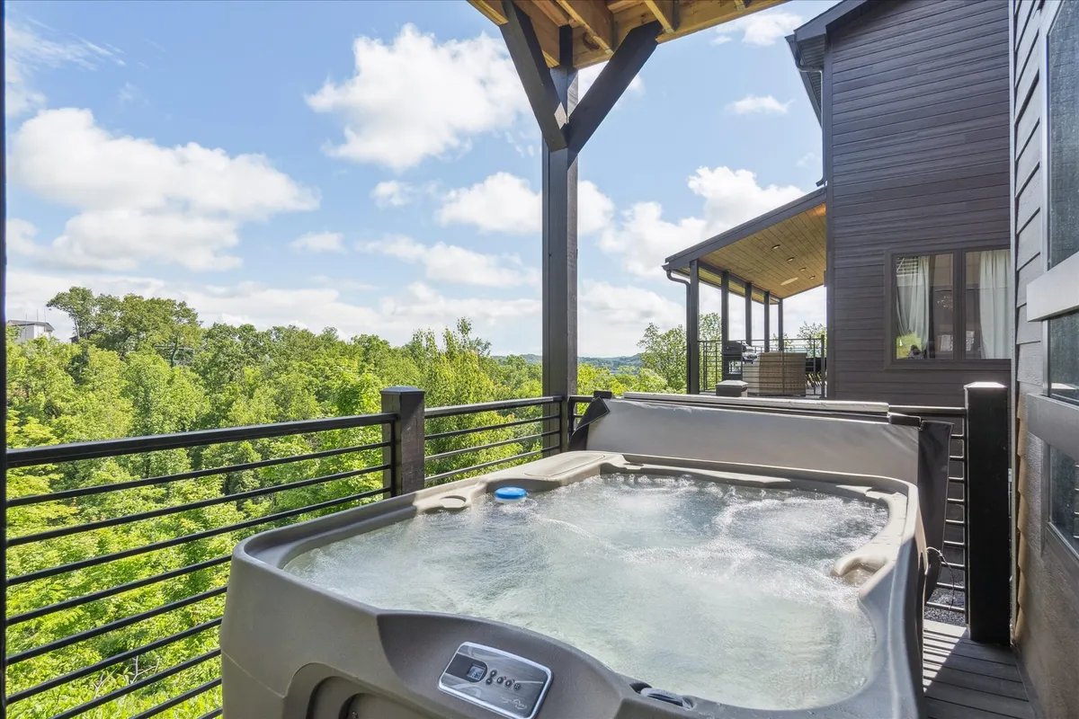 This image captures a beautiful exterior deck space featuring a hot tub with a lush green landscape and a wooden structure. The setting exudes serenity and the hot tub is perfectly positioned for guests to soak while taking in scenic views of the surrounding nature. The area is ideal for stargazing at night, enjoying sunsets, or relaxing with morning coffee.