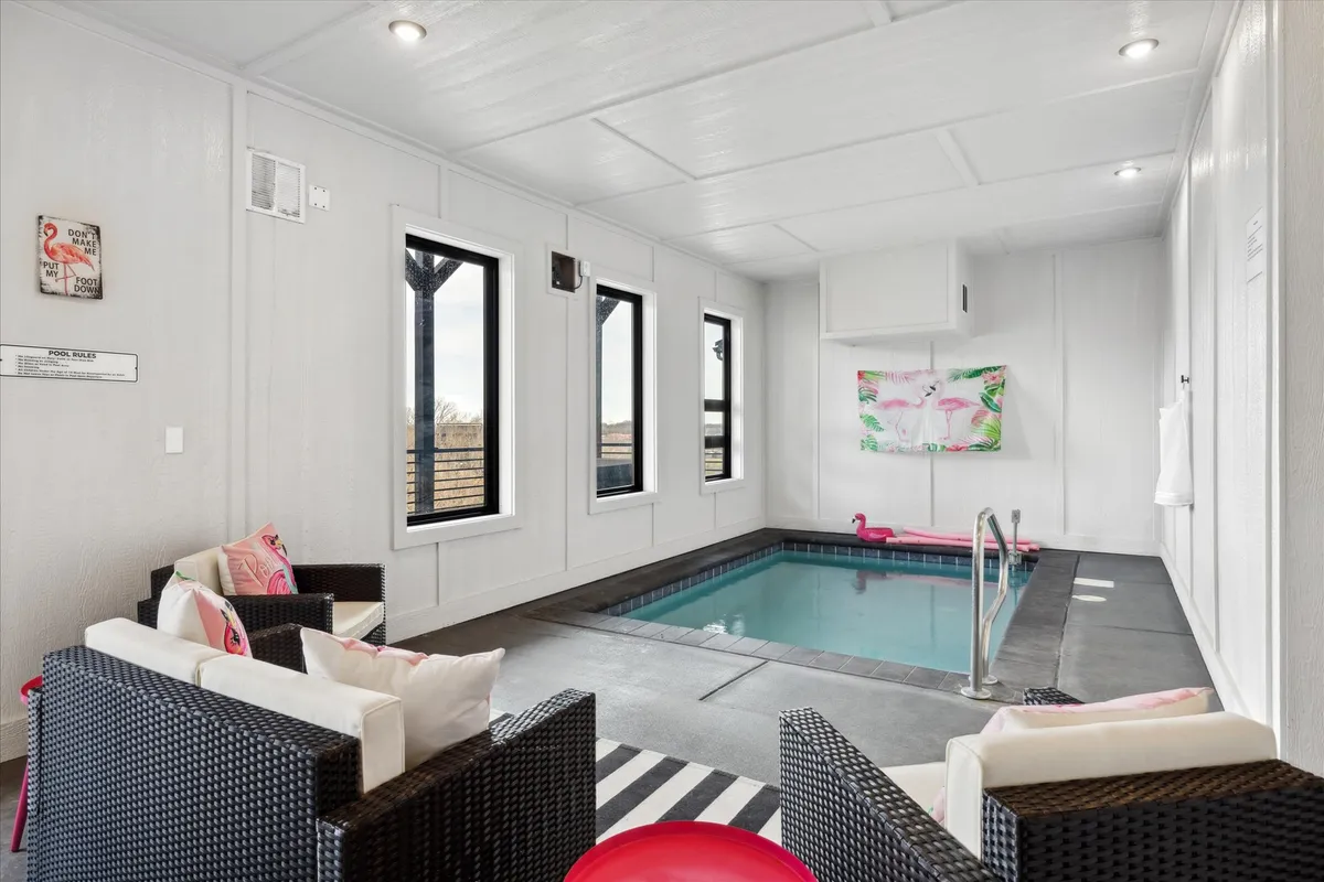 A vibrant indoor pool area featuring a sparkling pool, a colorful striped rug, a comfortable seating area, and lively wall art. Natural light streams in, inviting relaxation and play, while the setting suggests both family fun and moments of quiet enjoyment.