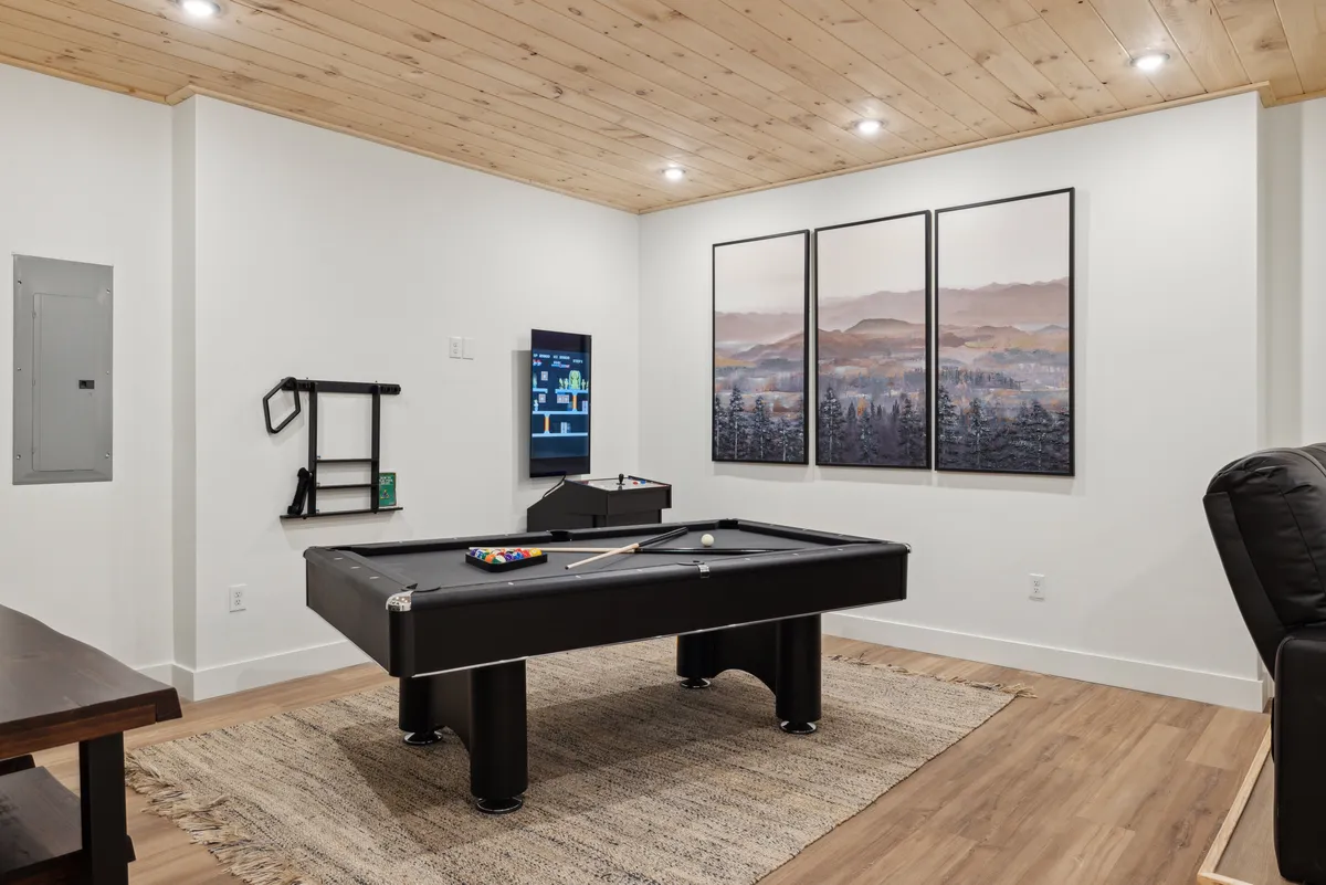 This interior image features a game room with a pool table, entertainment console, framed artwork, a rug, and a recliner. The atmosphere is casual and fun, perfect for friendly competitions and shared laughter. The room is designed for memorable game nights and group entertainment.