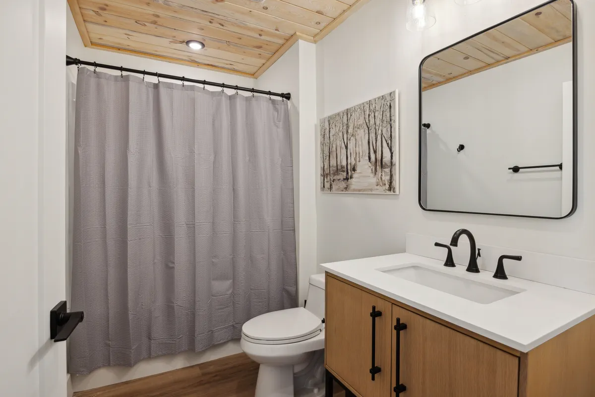 A modern bathroom featuring a spacious vanity with sink, a large mirror, an elegant shower curtain, and tasteful wall art. The atmosphere is calming and spa-like, echoing the 'spa-inspired baths' described in the section.