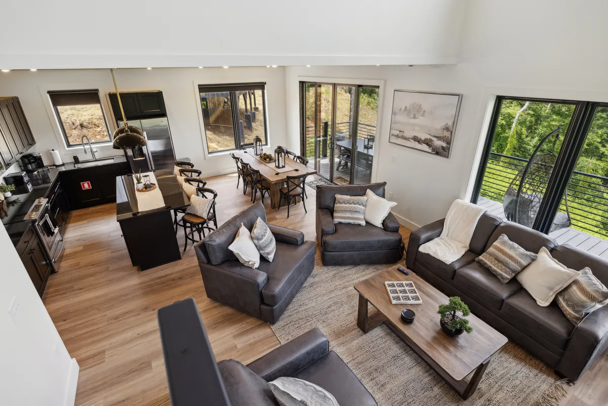 A spacious open-plan area featuring a comfortable seating arrangement, a dining table, a kitchen island, and large windows that brighten the entire space. The setup clearly connects the living, dining, and kitchen areas, inviting group activities and shared experiences.