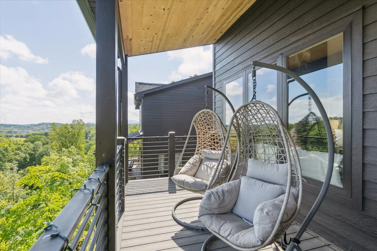 A beautifully appointed deck with hanging chairs overlooks a sweeping landscape of rolling hills and forest. The open-air setting is perfect for sunrise coffees or sharing evening stories, with the sturdy decking material and expansive views inviting guests to relax and connect with the outdoors.