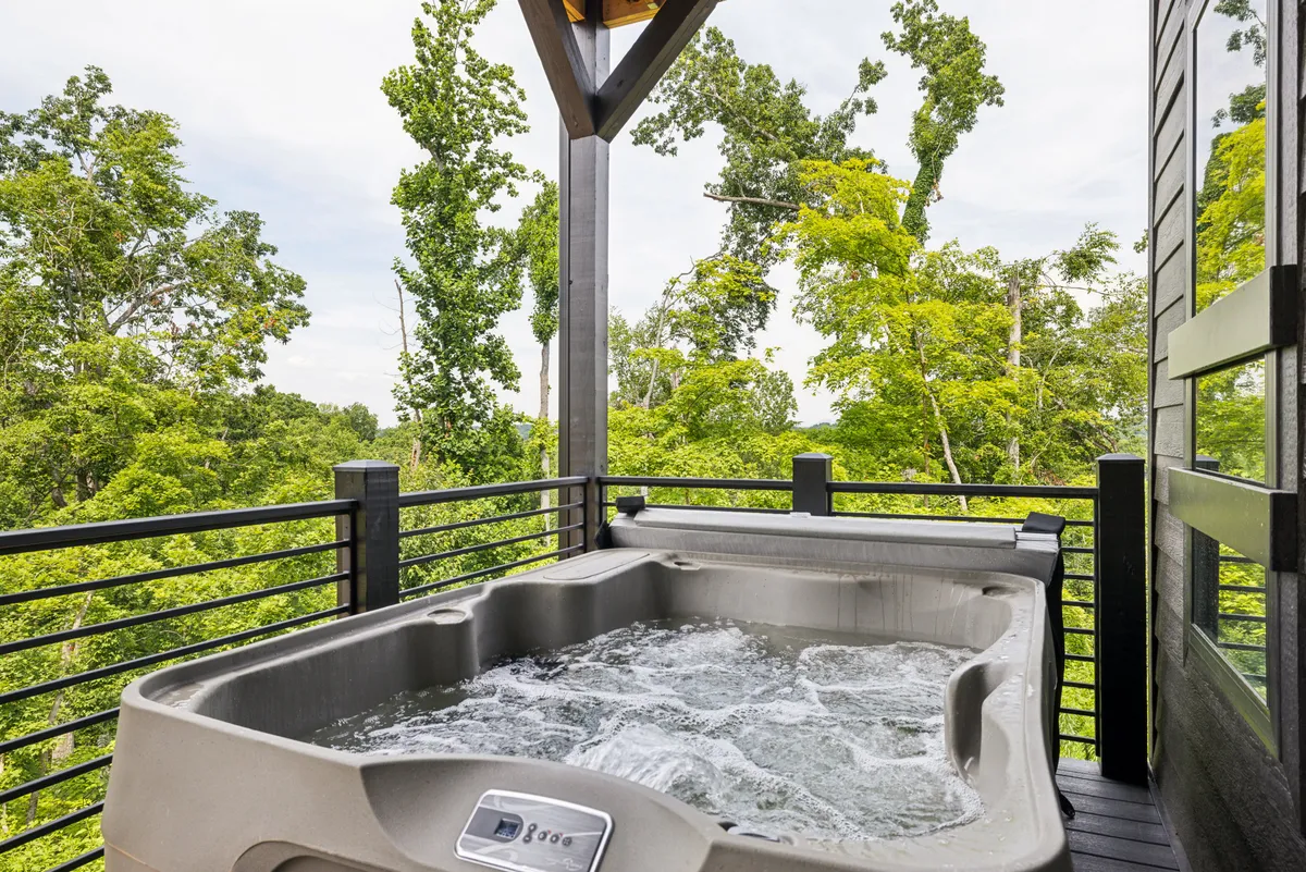 This image showcases an inviting hot tub set on a spacious deck, surrounded by lush greenery and trees. The view opens up to the natural landscape, with the hot tub positioned to take in the tranquil scenery. The setting exudes relaxation, ideal for stargazing or evening soaks after a day of mountain adventures.