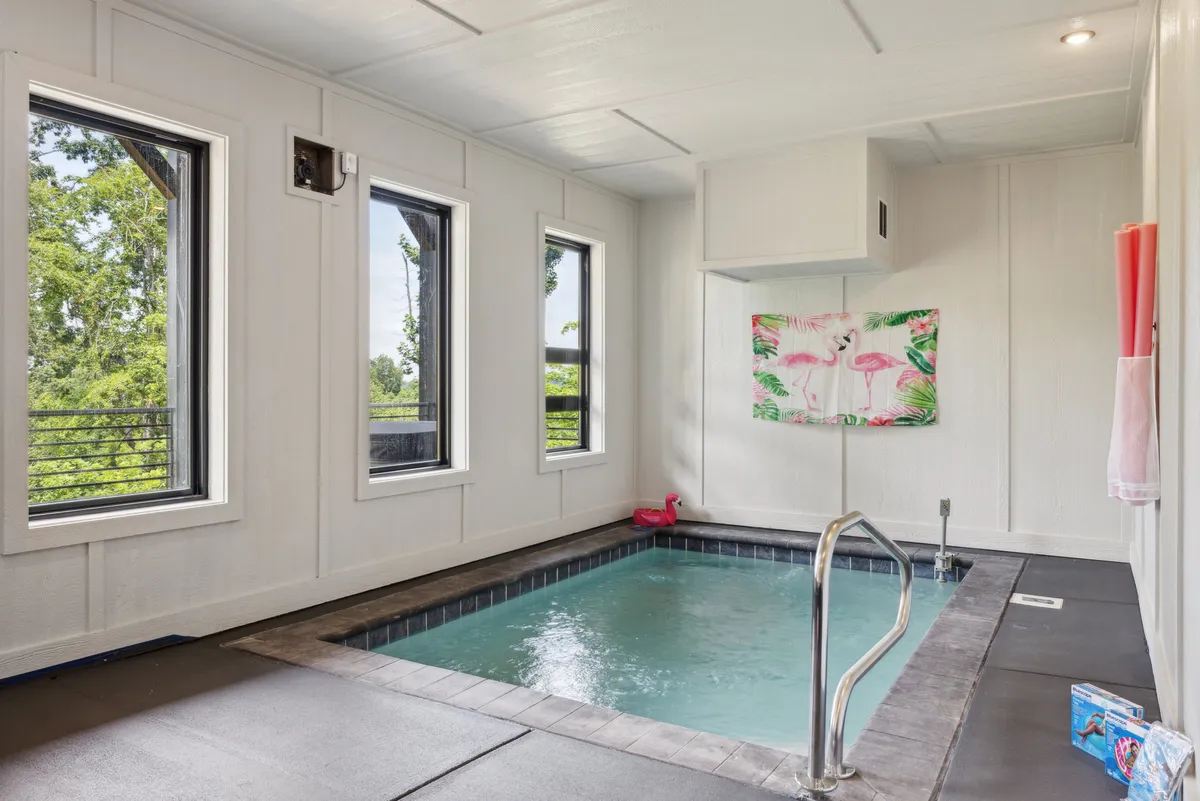 A stylish, small indoor pool framed by tropical artwork and large windows, allowing natural light to pour in. The space is ideal for private swims, relaxation, or small gatherings, offering guests a resort-style amenity in the privacy of their own home.