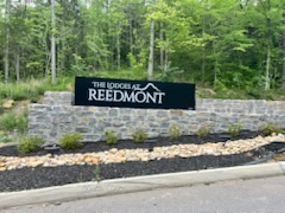 The image features the welcoming stone signage for The Lodges at Reedmont, set against a landscaped garden and surrounded by greenery. The entrance sets a tone of arrival and adventure, hinting at the resort’s proximity to nature and local attractions.